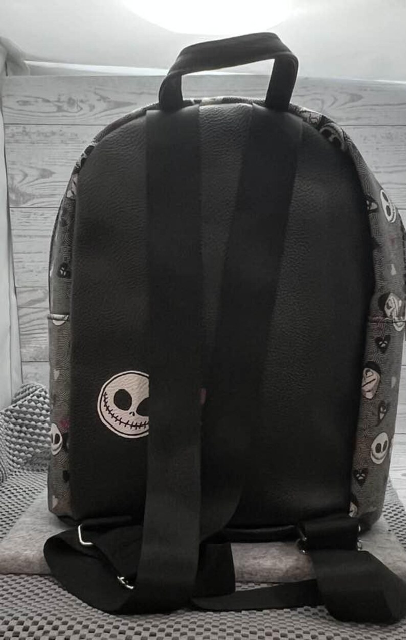 Puede incluir: Mochila negra con dise&ntilde;o de Jack Skellington. Tiene correas negras ajustables y un asa superior. El cuerpo principal es negro con un parche blanco con la cara de Jack Skellington. Los laterales tienen un patr&oacute;n repetido de Jack Skellington y otros personajes.