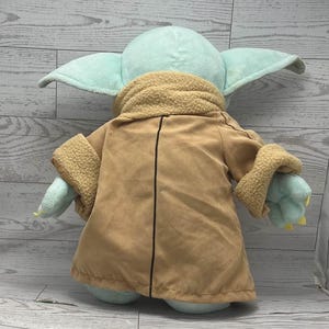 May include: A plush toy of a character with large ears, light green skin, and a tan coat with a fuzzy collar and cuffs. The toy is a soft, cuddly version of a popular character from a science fiction franchise.