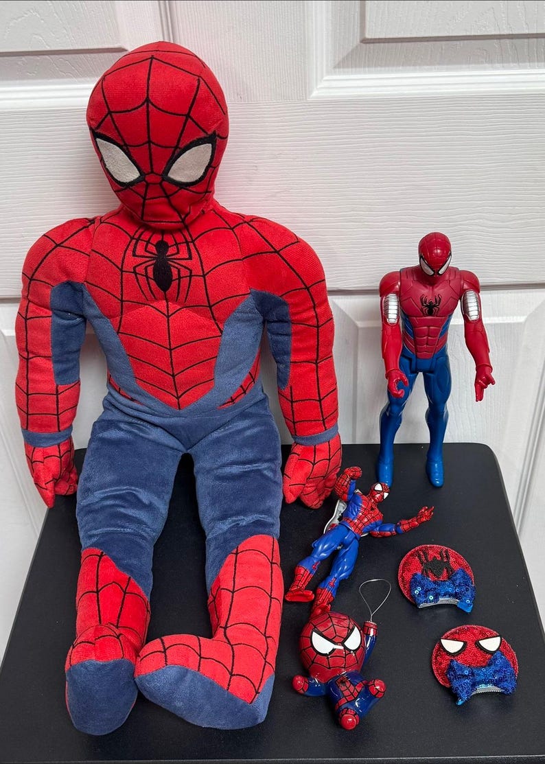 Puede incluir: Una colecci&oacute;n de juguetes y peluches con tem&aacute;tica de Spider-Man. La imagen presenta un gran mu&ntilde;eco de peluche de Spider-Man, una figura de acci&oacute;n de pl&aacute;stico y varios objetos decorativos m&aacute;s peque&ntilde;os, todos en la combinaci&oacute;n de colores rojo y azul caracter&iacute;stica del personaje.