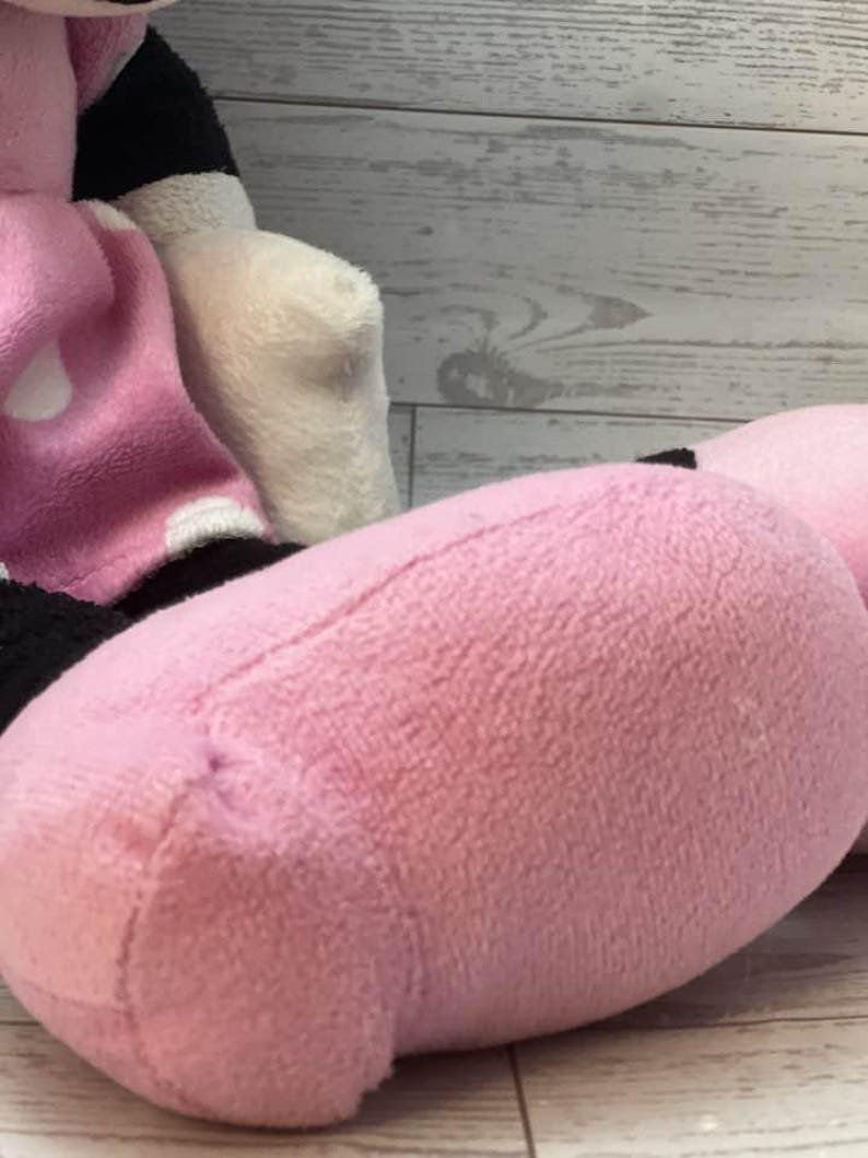 Pode incluir: Um brinquedo de pel&uacute;cia com um p&eacute; e uma perna rosa. O p&eacute; &eacute; rosa texturizado, com costuras vis&iacute;veis. O fundo inclui uma superf&iacute;cie de madeira branca e cinza. O brinquedo faz parte de um personagem maior.