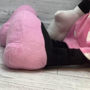 Pode incluir: Um brinquedo de pel&uacute;cia com um p&eacute; rosa e um p&eacute; preto. O p&eacute; rosa &eacute; grande e arredondado, com uma superf&iacute;cie macia e texturizada. O p&eacute; preto est&aacute; adjacente ao p&eacute; rosa. O fundo &eacute; uma superf&iacute;cie de madeira clara.