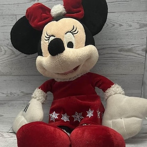 Puede incluir: Mu&ntilde;eca de peluche de Minnie Mouse con un vestido rojo con detalles de copos de nieve blancos y un lazo rojo a juego. La mu&ntilde;eca tiene orejas negras, una cara color crema y guantes blancos. Un art&iacute;culo festivo de vacaciones.