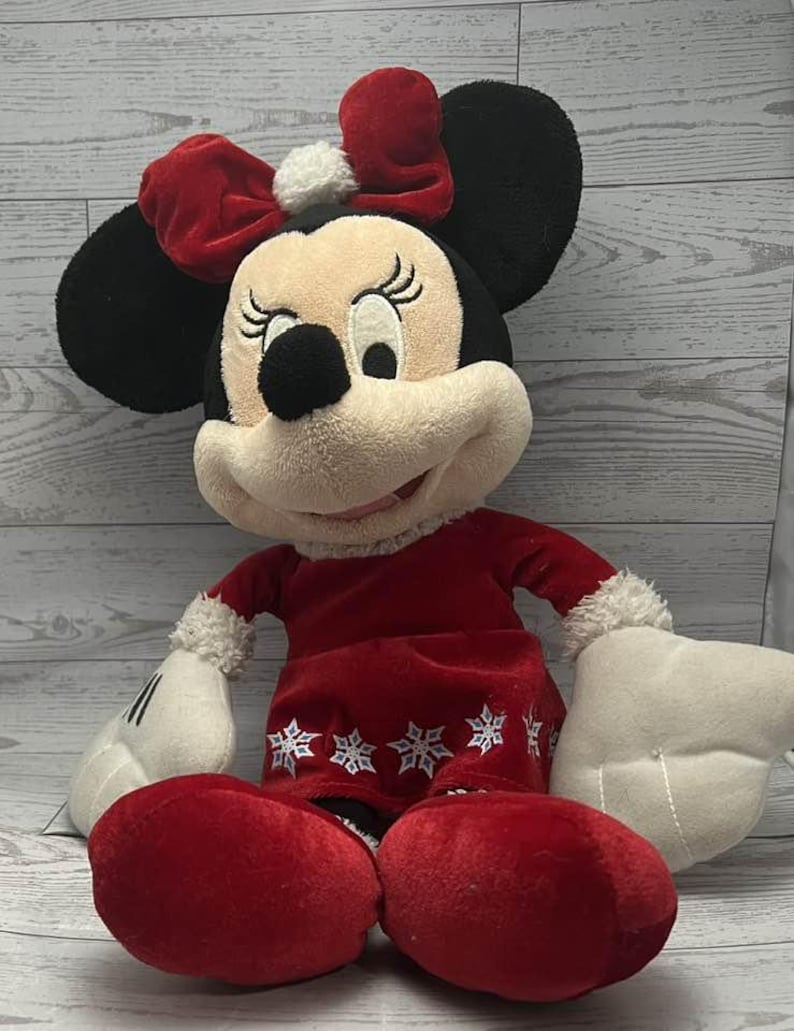 Puede incluir: Mu&ntilde;eca de peluche de Minnie Mouse con un vestido rojo con detalles de copos de nieve blancos y un lazo rojo a juego. La mu&ntilde;eca tiene orejas negras, una cara color crema y guantes blancos. Un art&iacute;culo festivo de vacaciones.