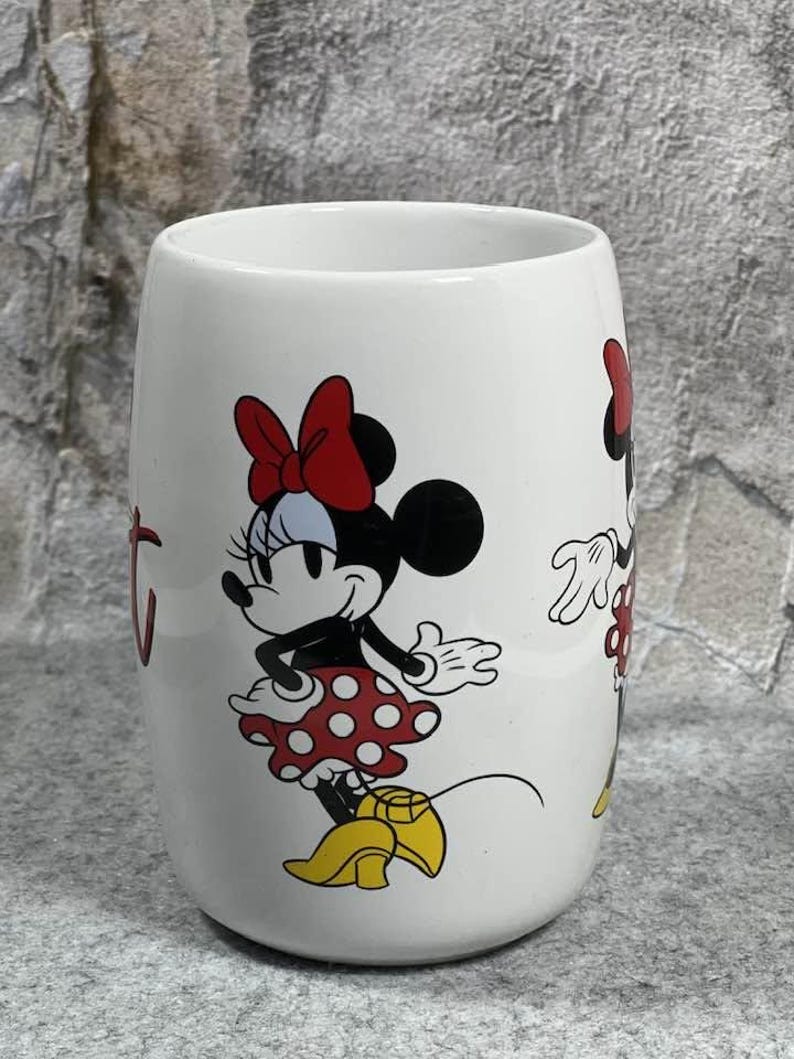 Pu&ograve; includere: Una tazza in ceramica bianca con una grafica di Minnie Mouse che indossa una gonna a pois rossi, un fiocco rosso e scarpe gialle. Il personaggio &egrave; raffigurato in piedi con una mano sul fianco. Il disegno &egrave; stampato sulla superficie esterna.