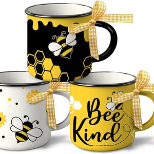 May include: Three enamel mugs with bee-themed designs. One mug is black with a yellow honeycomb pattern and a bee illustration. Another is white with a bee and flower design. The third is yellow with the words "Bee Kind". Each mug has a yellow gingham ribbon.