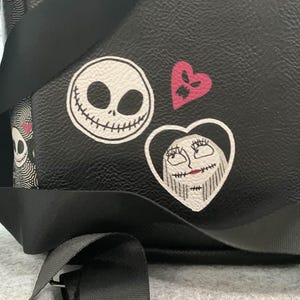 Puede incluir: Mochila negra con parches del rostro de Jack Skellington, el rostro de Sally en un coraz&oacute;n y un coraz&oacute;n rosa. La bolsa tiene correas negras y una hebilla plateada. El dise&ntilde;o es de la pel&iacute;cula "Pesadilla antes de Navidad".