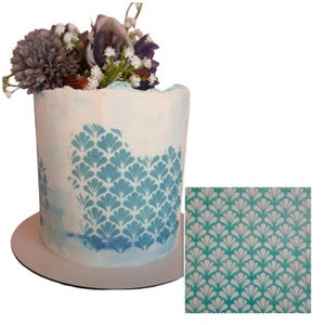 May include: A white cake decorated with a blue and white fan-shaped pattern. The cake is topped with a bouquet of flowers. A separate image shows a close-up of the stencil used to create the pattern.