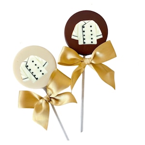May include: Two round chocolate lollipops with a white chef's jacket design. The lollipops are on sticks with gold ribbon bows.