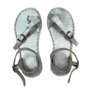 Peut inclure: Une paire de sandales argentées métallisées avec un design à boucle d'orteil, une bride de cheville réglable avec une boucle en métal et une semelle plate. Les sandales présentent une finition texturée sur la semelle intérieure et des coutures.