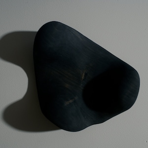 K&ouml;nnte beinhalten: Eine dunkelblaue, organisch geformte Holzschale mit einer glatten, abgerundeten Oberfl&auml;che und einer tiefen, kreisf&ouml;rmigen Vertiefung in der Mitte.