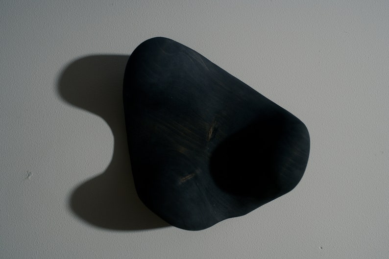 K&ouml;nnte beinhalten: Eine dunkelblaue, organisch geformte Holzschale mit einer glatten, abgerundeten Oberfl&auml;che und einer tiefen, kreisf&ouml;rmigen Vertiefung in der Mitte.