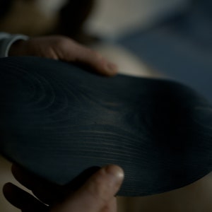K&ouml;nnte beinhalten: Eine dunkelblaue Holzschale mit einer glatten, abgerundeten Oberfl&auml;che und sichtbarer Holzmaserung.