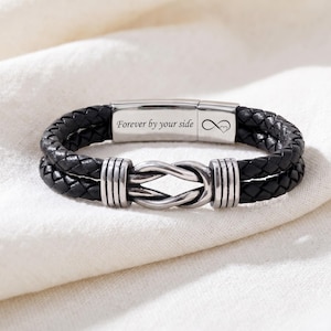 May include: Black braided leather bracelet with a silver clasp and knot design. The bracelet has the text "Forever by your side" and an infinity symbol with a heart. The bracelet is approximately 8 inches in length.