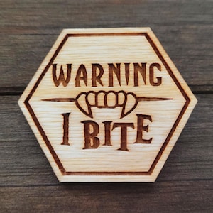 May include: A hexagonal wooden sign with the text "WARNING I BITE" and a stylized image of fangs.