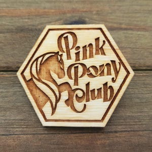 May include: A wooden hexagonal coaster with a laser-engraved design of a horse's head and the text "Pink Pony Club".