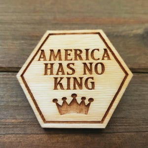 Puede incluir: Un letrero hexagonal de madera con el texto "AMERICA HAS NO KING" y un gráfico de corona.