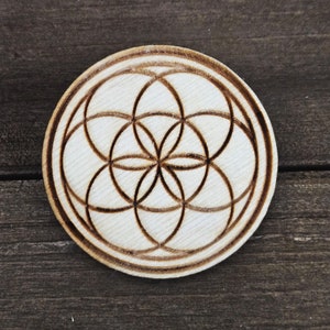 May include: A wooden coaster with a brown wood-burned design of a flower of life pattern.