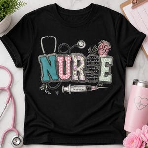 May include: A black t-shirt featuring the word NURSE in large, patterned block letters. The design includes a stethoscope, a syringe, a heart illustration, and small leaf accents. The letters have varied textures including floral, polka dot, and heartbeat patterns.