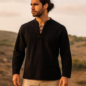 K&ouml;nnte beinhalten: Schwarzes Langarmhemd mit Schn&uuml;rhalsausschnitt. Das Hemd hat eine lockere Passform und ist aus einem weichen, strukturierten Stoff gefertigt. Das Hemd wird mit einer beigen Hose kombiniert.