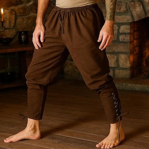 May include: Brown medieval-style pants with a drawstring waist and lace-up details on the lower legs. The pants are made of a soft fabric and are suitable for historical reenactments or themed events.