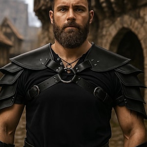 May include: Black leather shoulder armor with layered plates, worn over a black shirt. The armor features straps and metal accents. The image is set against a blurred background of a medieval town.