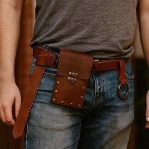 Puede incluir: Cintur&oacute;n de cuero marr&oacute;n con una funda a juego y un cierre decorativo. El cintur&oacute;n se lleva con vaqueros azules y tiene una correa larga colgando. La funda est&aacute; asegurada con remaches.