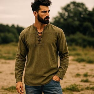 K&ouml;nnte beinhalten: Olivgr&uuml;nes Langarmhemd mit Schn&uuml;rhalsausschnitt. Das Hemd ist aus einem weichen, strukturierten Stoff gefertigt und wird mit einer blauen Jeans kombiniert. Das Hemd hat eine lockere Passform.