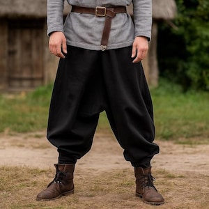 May include: A person wearing a gray long-sleeve shirt, a brown leather belt, and black pants. The person is also wearing brown leather boots with black laces. The outfit is suitable for historical reenactment or costume events.