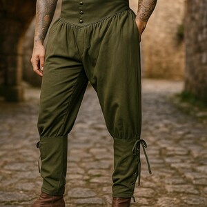 K&ouml;nnte beinhalten: Olivgr&uuml;ne Hose mit hoher Taille, Knopfleiste vorne und geraffter Taille. Die Hose hat eine lockere Passform an den Beinen und ist an den Kn&ouml;cheln mit B&auml;ndern gerafft. Die Hose ist aus einem weichen Stoff gefertigt und eignet sich f&uuml;r historische Nachstellungen oder Kost&uuml;me.
