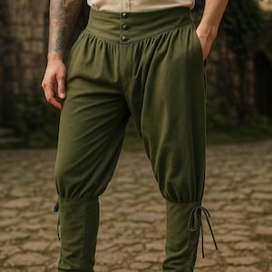 K&ouml;nnte beinhalten: Olivgr&uuml;ne Hose mit hohem Bund und Knopfdetails. Die Hose hat eine geraffte Taille und ist an den Kn&ouml;cheln mit Bindeb&auml;ndern versehen. Der Stil erinnert an historische oder Fantasy-Kleidung.