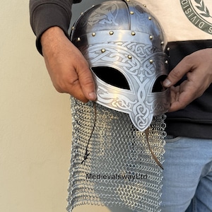 Peut inclure: Un casque viking en argent avec des motifs complexes en nœuds et une aventail de cotte de mailles. Le casque a une protection de nez pointue et est décoré de rivets en laiton.