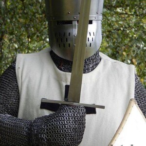 May include: A medieval knight's helmet and chainmail armor. The silver helmet has a visor with multiple eye slits. The knight is holding a sword and a small shield. The armor is set against a blurred green background.