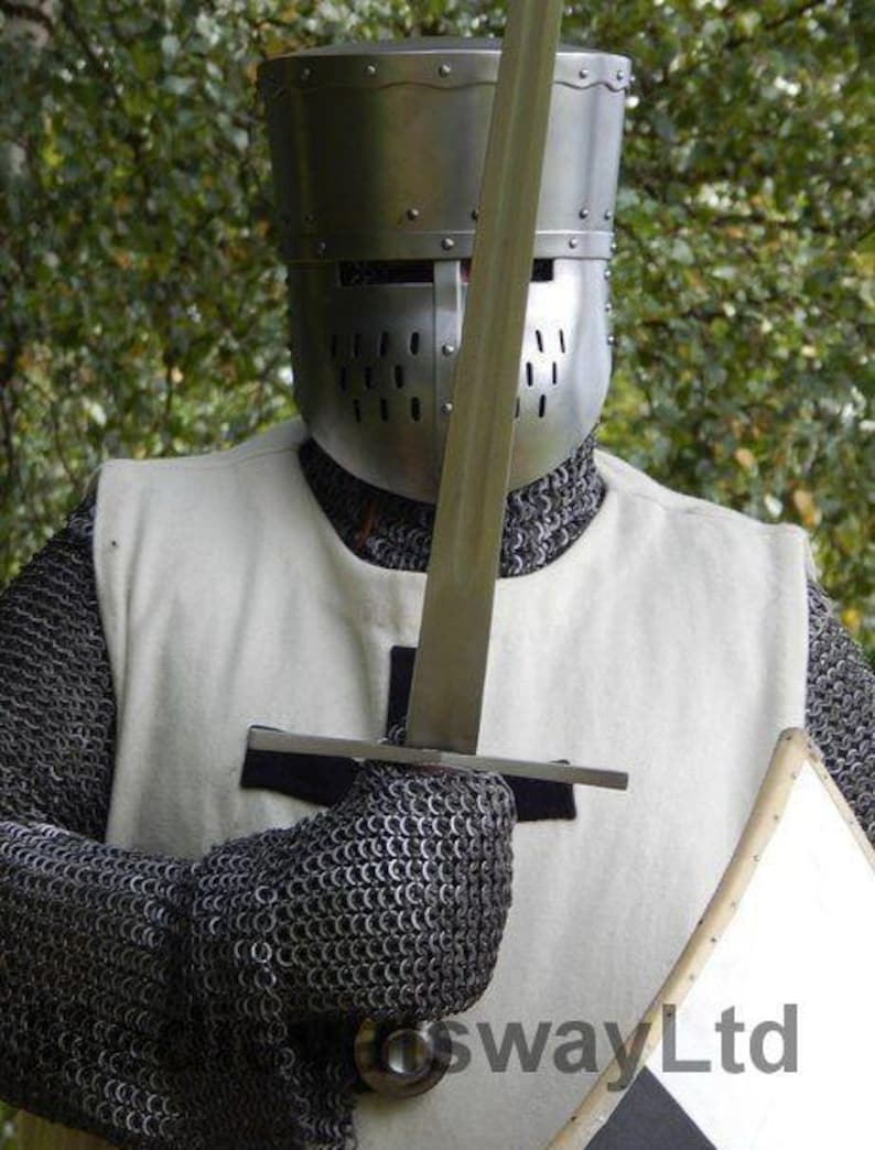May include: A medieval knight's helmet and chainmail armor. The silver helmet has a visor with multiple eye slits. The knight is holding a sword and a small shield. The armor is set against a blurred green background.