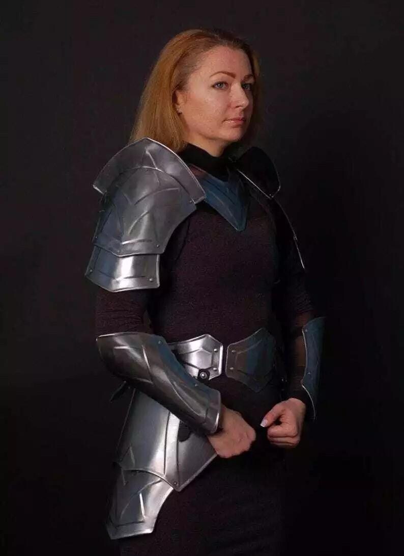 May include: A woman wearing silver armor with a black shirt and pants. The armor includes shoulder pads, bracers, and a belt.