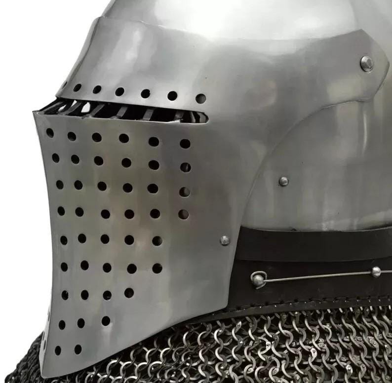 May include: A close-up of a medieval knight's helmet. The helmet is made of polished steel with a visor featuring numerous small holes for ventilation. A chainmail collar is visible at the base, providing neck protection. The design is historically accurate.