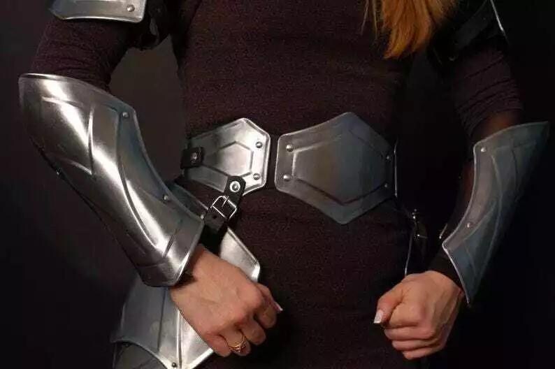 May include: A silver metal armor set with a chest plate, arm guards, and a belt. The armor is worn by a person with long, blonde hair.
