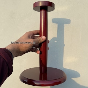May include: A dark red wooden hat stand with a round base and a tall, cylindrical post. The stand is designed to hold a hat on top of the post.