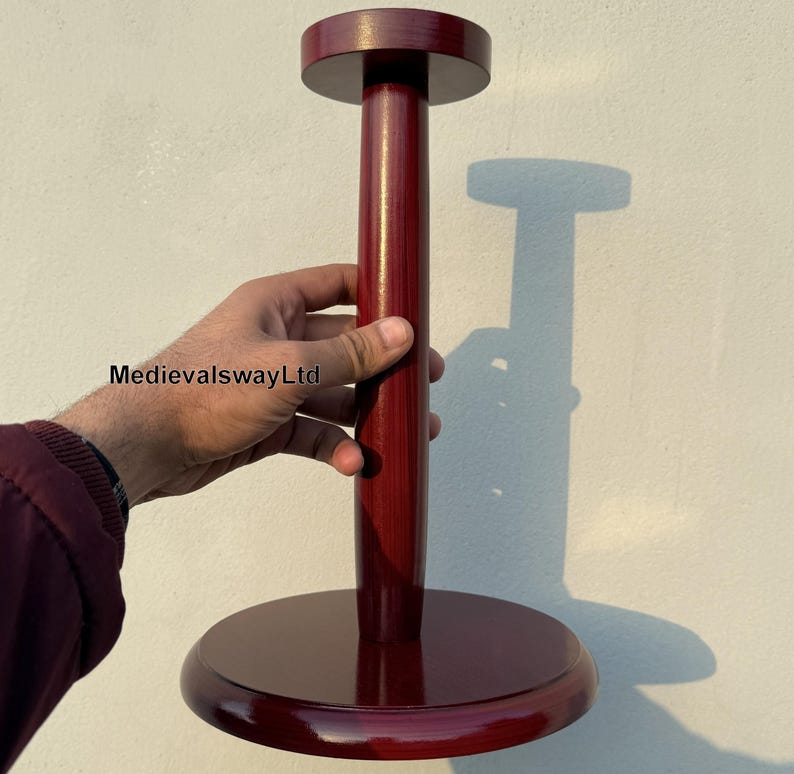 May include: A dark red wooden hat stand with a round base and a tall, cylindrical post. The stand is designed to hold a hat on top of the post.
