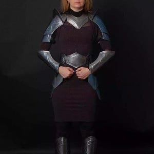 May include: A woman wearing silver and blue armor with a dark dress and boots.