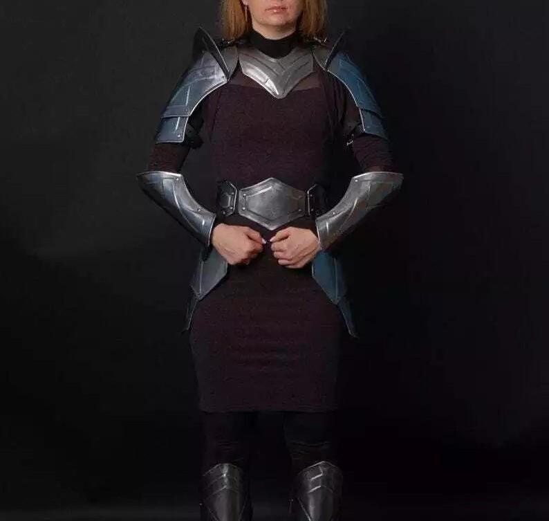 May include: A woman wearing silver and blue armor with a dark dress and boots.