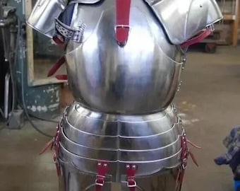 May include: A silver metal suit of armor with red leather straps. The armor is made up of a breastplate, shoulder pads, and a skirt. The armor is displayed on a wooden stand.