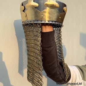 May include: A medieval style helmet with a chainmail coif. The helmet is made of metal and has a brass crown with a pointed top. The chainmail coif is made of small metal rings linked together.