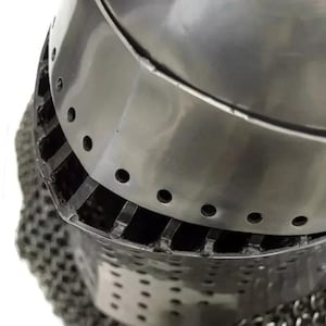 May include: Close-up of a medieval steel helmet with a polished finish. The helmet features a rounded top with a series of small, evenly spaced holes and a lower section with vertical slits and chainmail.
