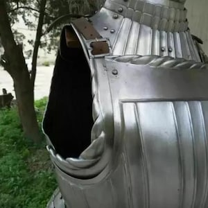 May include: A silver metal breastplate with a leather strap and decorative details. The breastplate is made of metal plates that are joined together. The breastplate is a type of armor that was worn by soldiers in the past.
