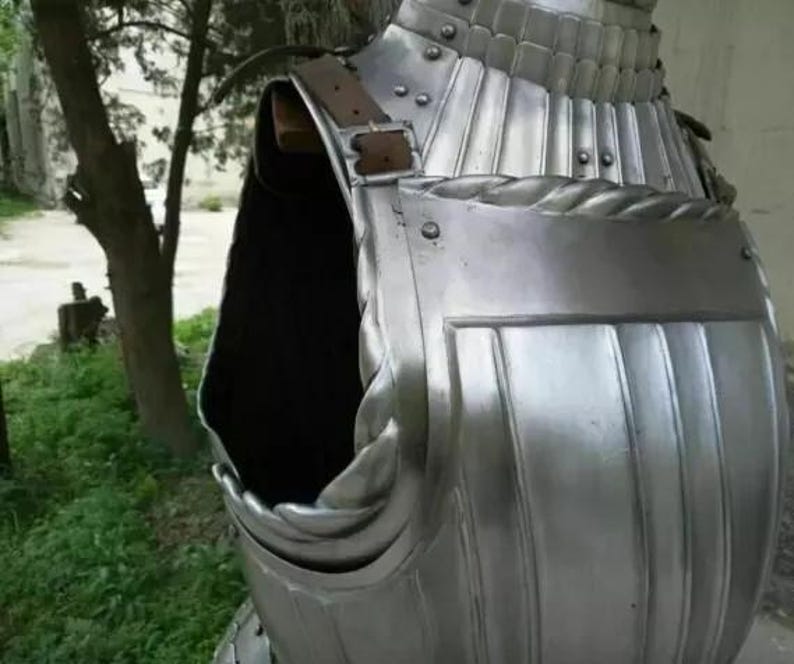 May include: A silver metal breastplate with a leather strap and decorative details. The breastplate is made of metal plates that are joined together. The breastplate is a type of armor that was worn by soldiers in the past.
