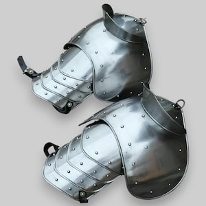 May include: A pair of silver metal medieval arm guards with rivets and leather straps. The guards are made of metal plates and are designed to protect the wearer's arms during combat.