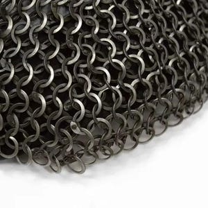 May include: Close-up of a section of chainmail armor. The metal rings are interlocked in a dense pattern, creating a flexible, protective surface. The color is a dark, metallic gray, with a slight sheen. The background is a dark fabric.