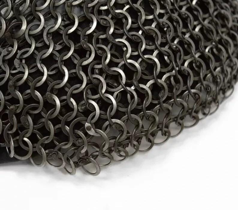 May include: Close-up of a section of chainmail armor. The metal rings are interlocked in a dense pattern, creating a flexible, protective surface. The color is a dark, metallic gray, with a slight sheen. The background is a dark fabric.