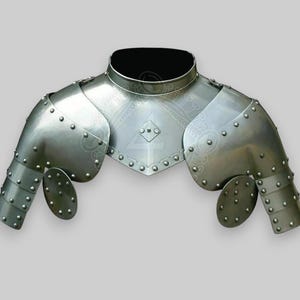 Könnte beinhalten: Silberfarbener Metallschulterpanzer mit dekorativem Design und Nieten. Die Rüstung besteht aus mehreren Platten und hat einen Nackenschutz.