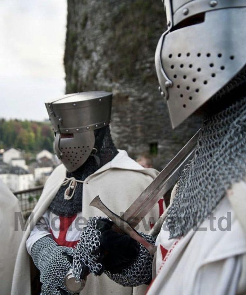 May include: Two medieval knights in full armor, including helmets, chainmail, and white capes with red crosses. One knight holds a sword. The image is set against a blurred background of a stone structure and foliage.
